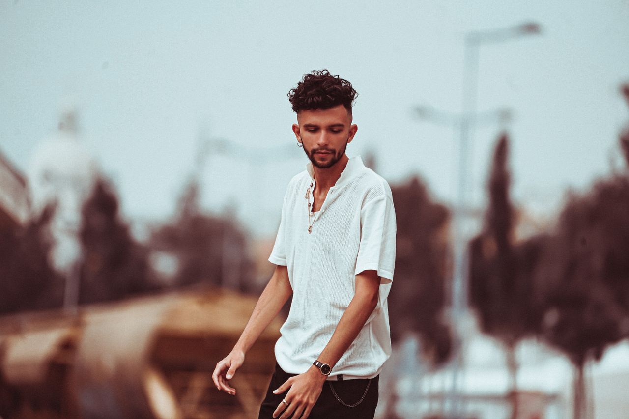 A fashionable young man in a white shirt poses in a blurred urban environment.